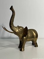 Front left angle view of the large brass elephant figurine showing trunk raised and tusks extending outward.