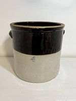 Front view of vintage stoneware crock showing two-tone beige and brown color with a blue number 4 stamped on the front. Crock has side loop handles.