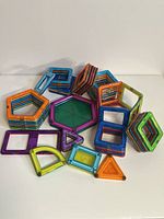 Multiple geometric magnetic building tiles in various colors stacked and spread on surface.