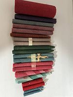 Multiple rolled beeswax taper candles in colors like red, purple, green, blue, beige, brown arranged on a white surface in bundles and loose