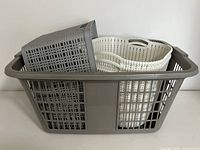 Front side view of large grey laundry basket containing smaller grey and two white baskets inside, showing size differences and handle design.