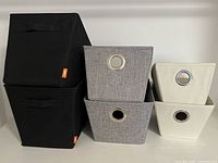 Front view of 6 fabric storage bins stacked and arranged showing black, grey, and beige colors with handles.