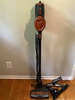Full view of Shark Rocket upright stick vacuum standing against wall with accessories arranged on floor beside it.
