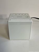 Front view of white Sony digital alarm clock radio cube, showing smooth display face with no buttons.