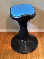 Blue foam padded seat with black plastic edges, black fabric covered column, circular black metal base with lock switch. Seat 12 inches wide, base 17 inches wide, total height 22 inches.