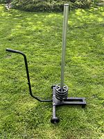 Side view of black metal tire stand on grass, showing vertical silver pole and black wheels with curved handle.