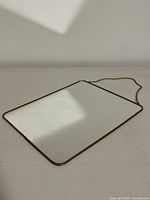 Rectangular hanging mirror with brass-tone metal frame laid flat showing reflective surface.