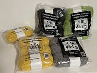 Photo showing multiple skeins of yellow, green, black, and gray cotton blend yarn in clear packaging labeled 'Surplus Promotion' with weight marked as 1 lb (454 g) per package.