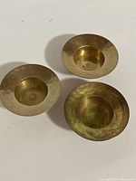 Three vintage brass tealight candle holders viewed from above, showing circular rims and recessed candle cups. Brass patina and signs of oxidation visible.