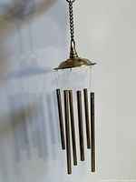 Front view of the vintage brass wind chime hanging from a chain showing six brass rods suspended from a rounded brass top piece.