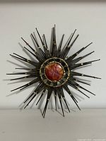 Full front view of the vintage Brutalist starburst metal wall art showing radiating metal spikes and central reddish-brown circular element.