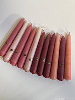Full view of 11 tapered candles in various shades from light pink to deep red with small Colonial Candle stickers visible on some.