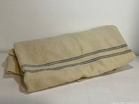 Folded cream wool blanket with horizontal dark gray stripes displayed on a flat white surface.