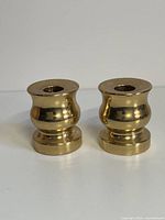 Front view of two vintage brass candle holders with reflective, rounded midsections and flat bases and tops