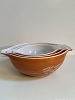 Stacked view of three Pyrex Autumn Harvest orange Cinderella bowls, showing spout and handle design.