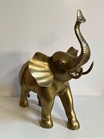 Full side front view of extra large brass elephant figurine standing with raised trunk and visible details of ears, eyes, and tusks.