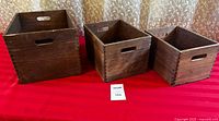 Three dark wood nesting boxes lined up from largest to smallest, showing exterior sides with handle cut-outs and finger joints.