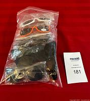Bag containing 8 pairs of promotional sunglasses in plastic bags, showing colors like black, white, and orange