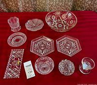 Wide view of assorted lead crystal and cut glass pieces including large bowl, plates, dish, candle holder, and vase arranged on red fabric