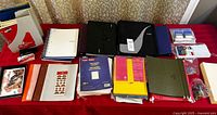 Overview of assorted office stationery including binders, notebooks, paper packs, clips, envelopes, stapler, and folders on a red tablecloth.