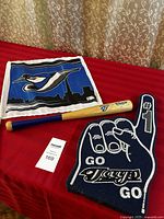 Photo displaying all three items in the Blue Jays fan kit on a red surface: flag, mini bat, and foam finger.