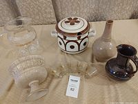 Brown and white ceramic soup terrine with lid, three unique vases of different sizes and colors, five shot glasses with leaf pattern arranged on a table