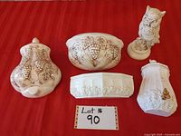 Five ceramic items displayed on a red cloth: two wall planters with grapevine patterns, two wall ornaments, and an owl figurine on a pedestal.