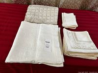 Full lot arranged on red surface showing largest folded linens including tablecloth and lace overlay, as well as stacks of napkins.