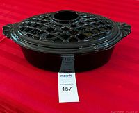 Black enamel woodstove pot with lattice-pattern lid placed on a red surface, showing the exterior and design details.