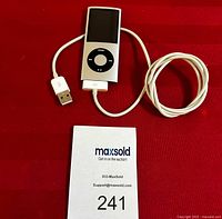 Apple iPod Nano 8GB with charging cable laid on red background, showing front and cable details.