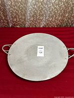 Top view of the round aluminum tray showing surface texture and two metal handles on sides.