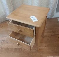 Light wood solid end table with two drawers open showing interior wood and smooth top surface.