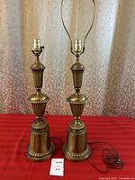 Pair of tall vintage brass table lamps with electrical cords on red cloth, 25 inches high.