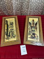 Two matching wood framed prints with European street scenes. Frames have a medium brown wood finish, prints sized around 18.5 by 9.5 inches.