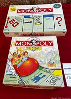 Photo showing both the Monopoly Classic and Monopoly Junior board games in their original boxes on red cloth background.