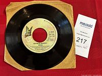 Photo of the Queen 45 RPM vinyl single with the song "Bohemian Rhapsody" labeled, showing the record in a brown paper sleeve and a MaxSold lot tag.
