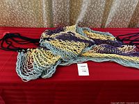 Multi-colored rope hammock laid out showing intertwined blue, cream, and purple ropes forming the netting.