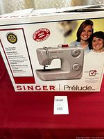 Box front showing image of Singer Prelude sewing machine with two women in background plus key features and 25 year limited warranty badge