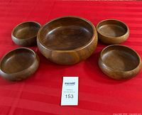 Five solid dark wood salad bowls arranged on a red cloth, one large bowl in center and four smaller bowls surrounding it.