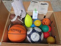 Box containing Cooper knee and shin pads and various sports balls including basketball, soccer ball, bocci balls, and footballs