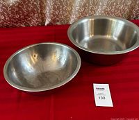 Two stainless steel mixing bowls placed on red fabric surface against a curtain background to show overall size and condition.