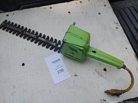 Green vintage electric hedge trimmer lying on white surface with a Masold auction card labeled 236 beside it, showing full view of the blades and handle.