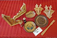 Overall lot contents arranged on red fabric including carved wooden plates, salt and pepper shakers, bowl, wooden oven rack tool, and carved ornamental corner pieces.