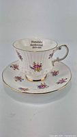 Photo of commemorative bone china cup and saucer, white with floral decorations and gold trim. Cup shows printed 'Manitoba Centennial 1870-1970' inside.