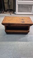 Front view of handmade wooden stained step stool showing top and side panel with open storage space below step.