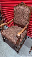 Front and side angled view of vintage wooden armchair with patterned upholstery and carved top rail.