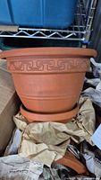 Four terra cotta plant pots with matching saucers, showing one pot close up resting on its saucer with decorative Greek key pattern.