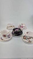 Photo of all five bone china tea cups with matching saucers, each with unique floral or fruit designs and gold trim.