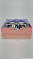 Front view of silver cuff bracelet with square blue synthetic stone setting in box.
