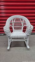 Front view of white painted wicker rocking chair with curved armrests and rounded woven lattice backrest, sitting on rocking wooden bases.